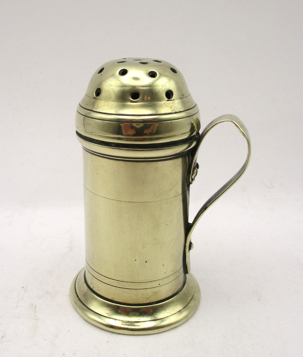 An eighteenth-century brass spice dredger featuring a perforated domed lid, a cylindrical body with moulded bands, a curved strap handle, and a stepped circular base. View II