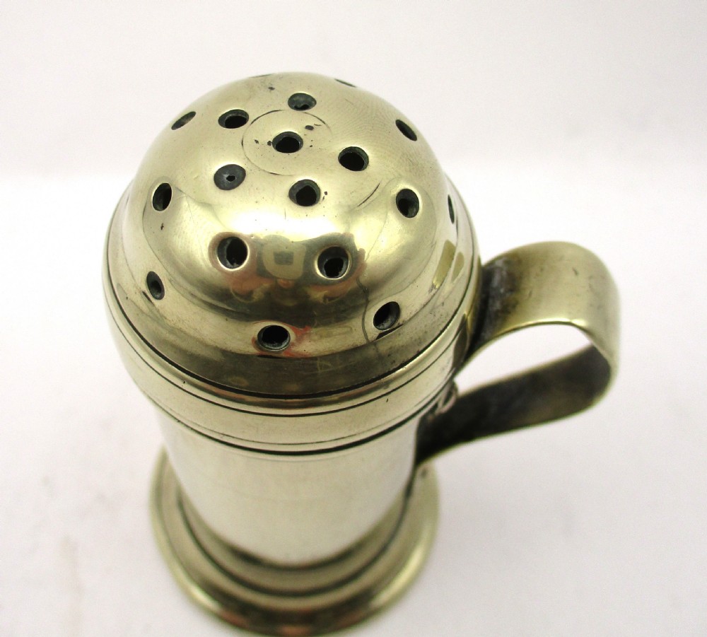 An eighteenth-century brass spice dredger featuring a perforated domed lid, a cylindrical body with moulded bands, a curved strap handle, and a stepped circular base. View III