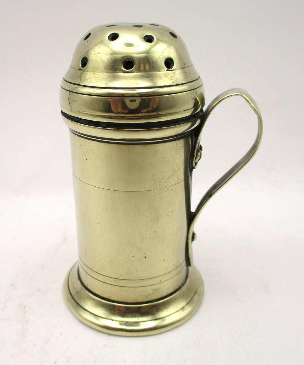 An eighteenth-century brass spice dredger featuring a perforated domed lid, a cylindrical body with moulded bands, a curved strap handle, and a stepped circular base. View IV