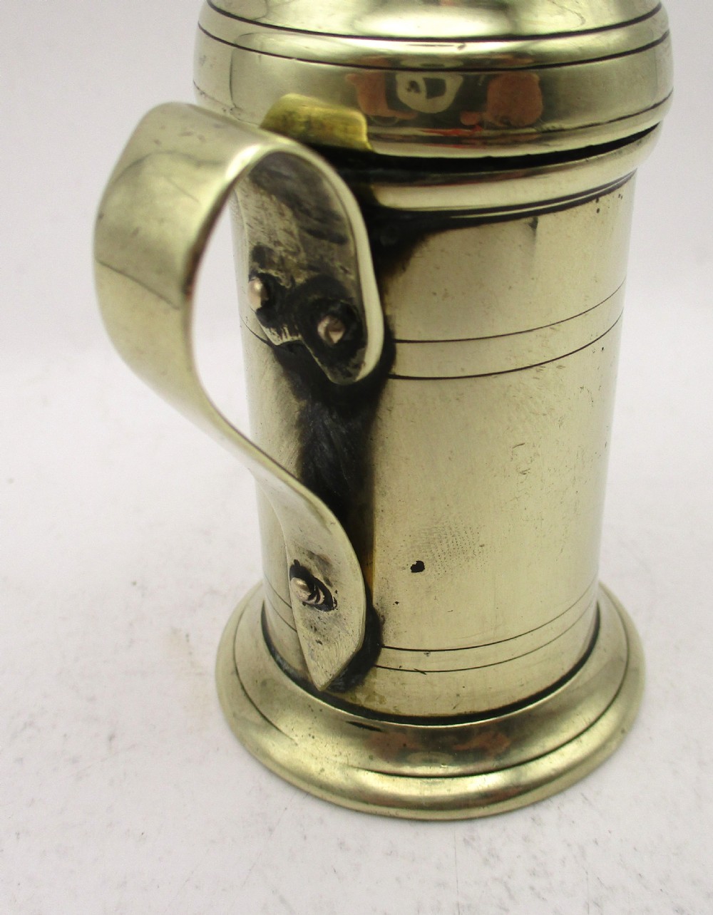 An eighteenth-century brass spice dredger featuring a perforated domed lid, a cylindrical body with moulded bands, a curved strap handle, and a stepped circular base. View VIII