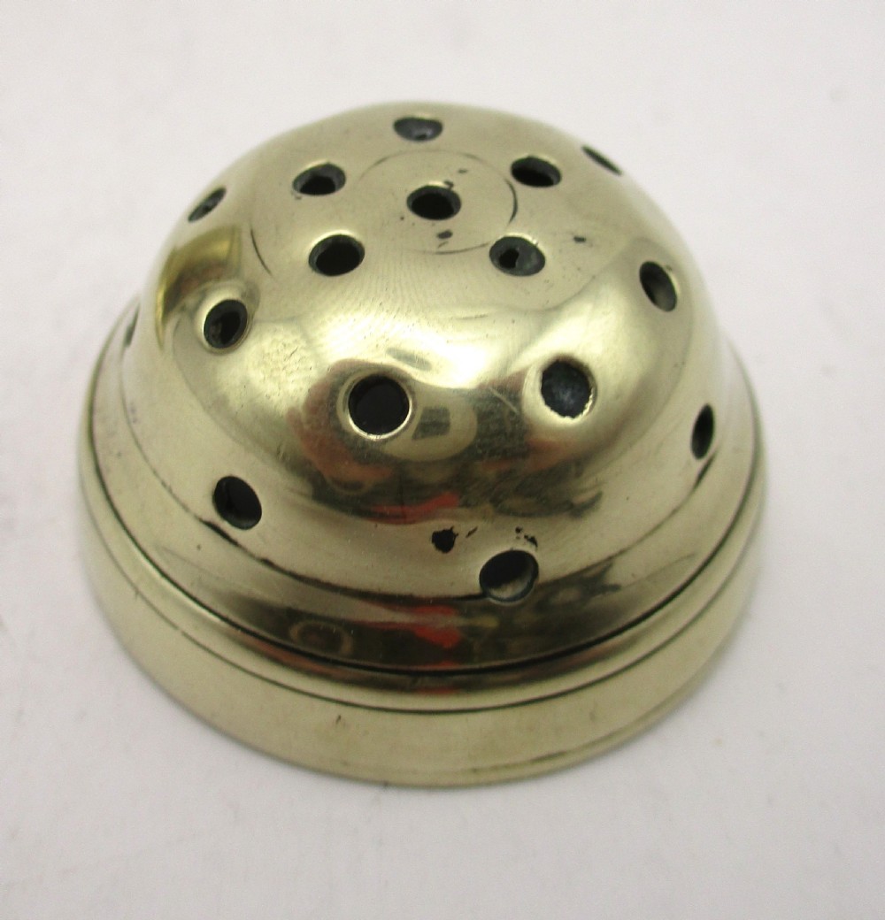 An eighteenth-century brass spice dredger featuring a perforated domed lid, a cylindrical body with moulded bands, a curved strap handle, and a stepped circular base. View X