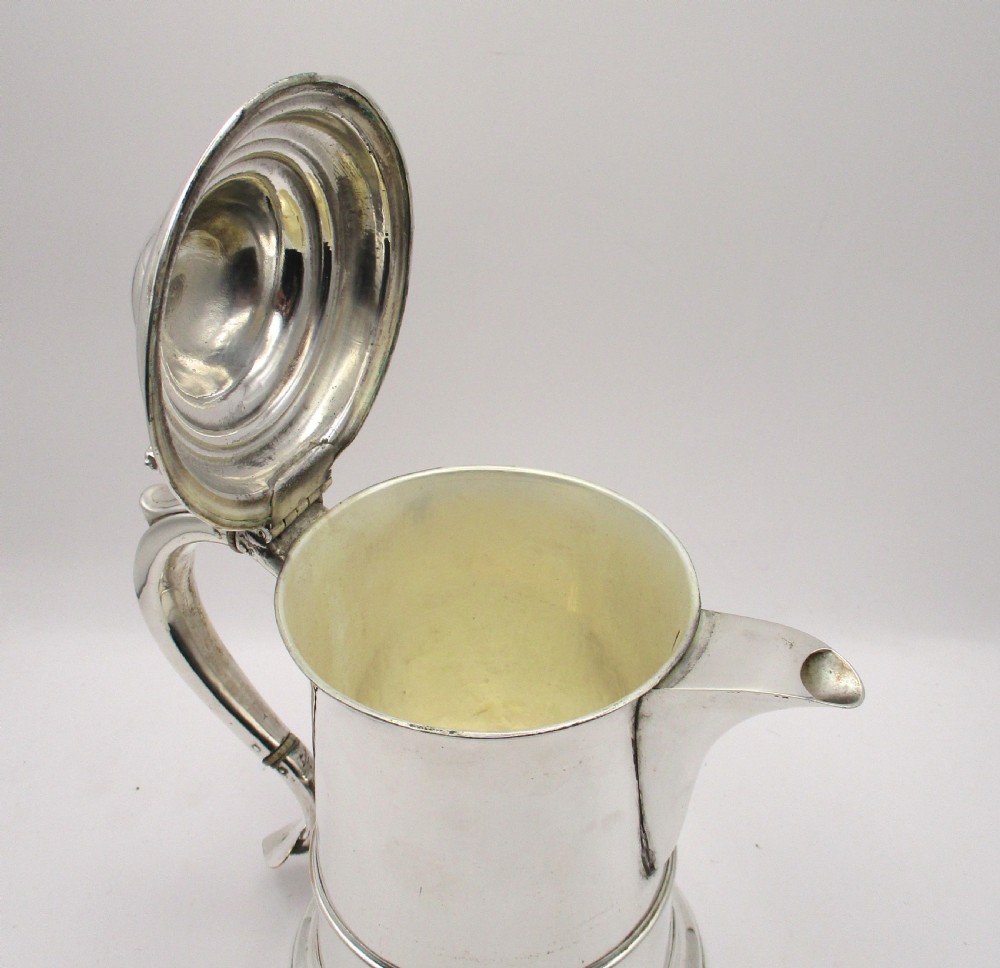 An 18th-century silver-plated beer jug with a domed hinged lid, thumbpiece, spout, and curved scroll handle. View X