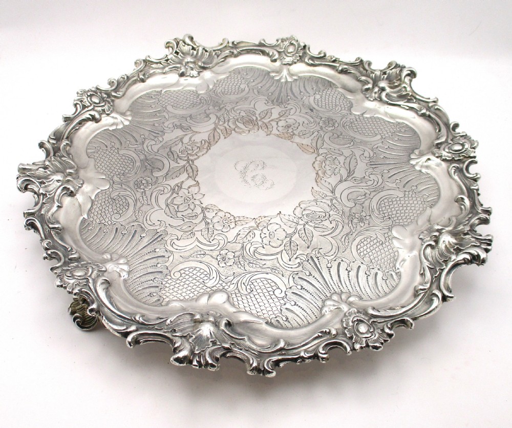 A circular Victorian Sheffield silver-plated serving tray featuring an ornate Rococo scroll border and intricate floral engraving across the flat surface.
