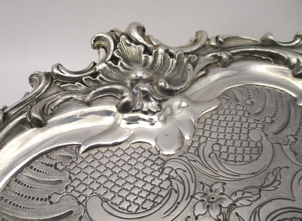 A circular Victorian Sheffield silver-plated serving tray featuring an ornate Rococo scroll border and intricate floral engraving across the flat surface. View V