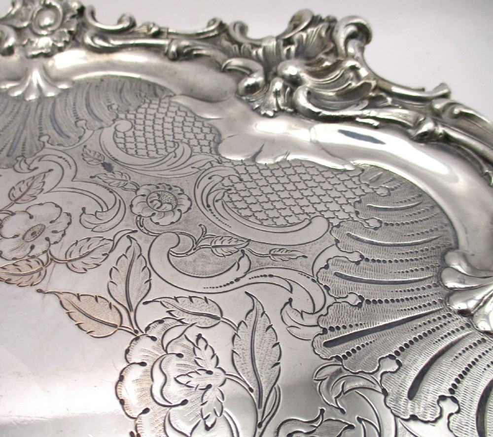 A circular Victorian Sheffield silver-plated serving tray featuring an ornate Rococo scroll border and intricate floral engraving across the flat surface. View VI