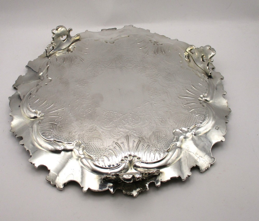 A circular Victorian Sheffield silver-plated serving tray featuring an ornate Rococo scroll border and intricate floral engraving across the flat surface. View VIII