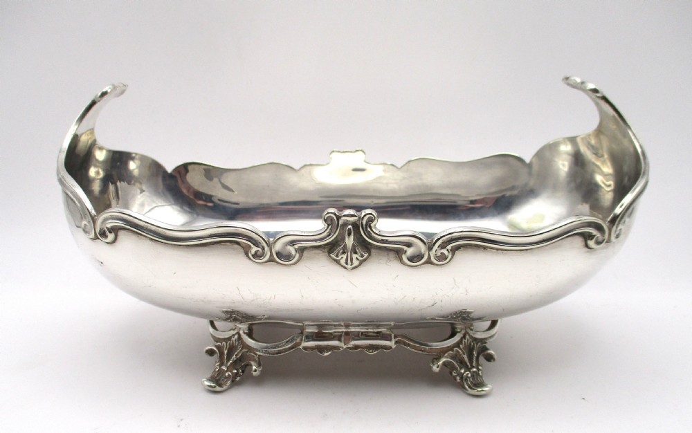 An Art Nouveau silver-plated boat-shaped bonbon dish featuring curved side handles, a decorative scrolled rim, and four cast scroll feet.