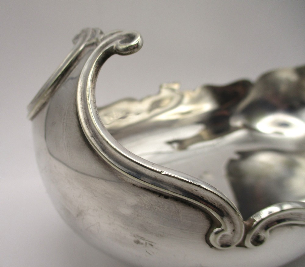 An Art Nouveau silver-plated boat-shaped bonbon dish featuring curved side handles, a decorative scrolled rim, and four cast scroll feet. View IV