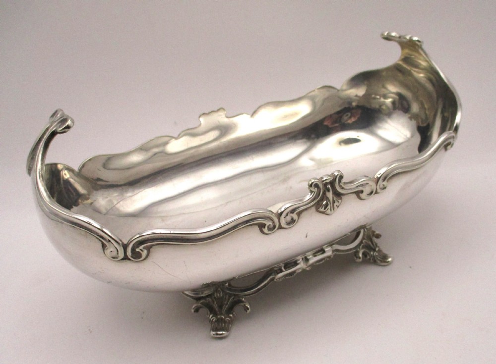 An Art Nouveau silver-plated boat-shaped bonbon dish featuring curved side handles, a decorative scrolled rim, and four cast scroll feet. View VII