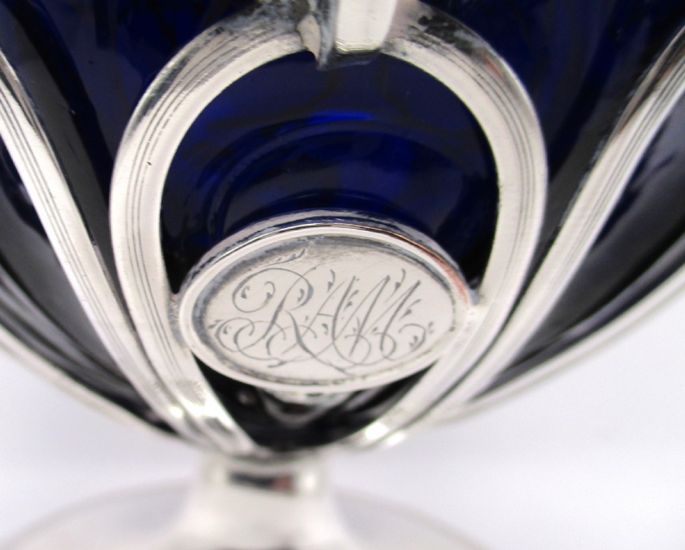 A Georgian Sheffield plated silver wirework sugar basket featuring an oval engraved cartouche, overhead handle, pedestal foot, and cobalt blue glass liner. View III