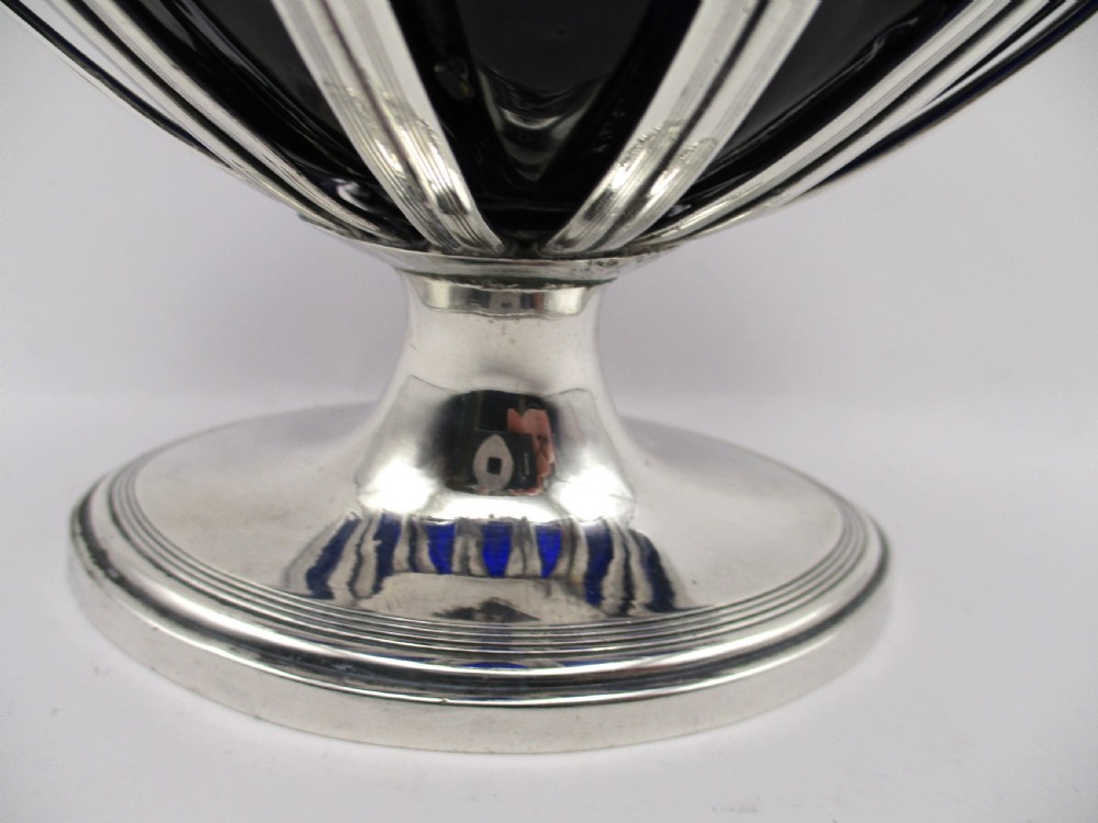 A Georgian Sheffield plated silver wirework sugar basket featuring an oval engraved cartouche, overhead handle, pedestal foot, and cobalt blue glass liner. View V