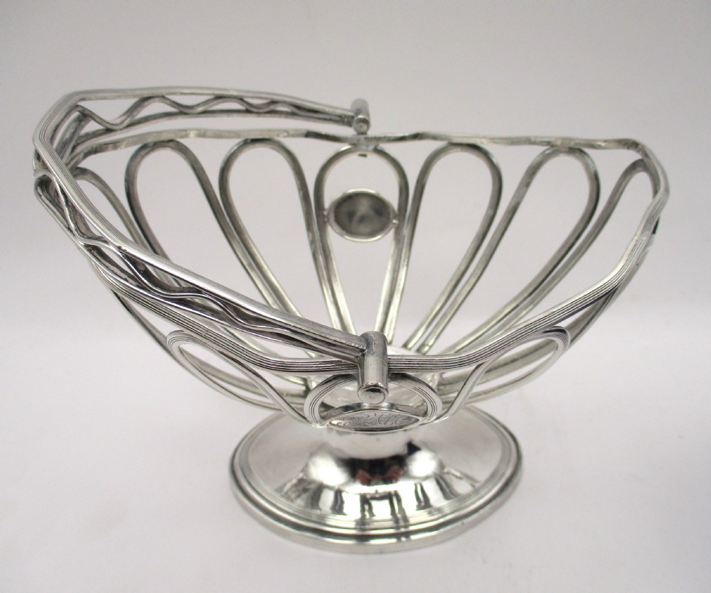 A Georgian Sheffield plated silver wirework sugar basket featuring an oval engraved cartouche, overhead handle, pedestal foot, and cobalt blue glass liner. View IX