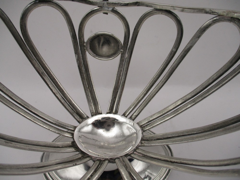 A Georgian Sheffield plated silver wirework sugar basket featuring an oval engraved cartouche, overhead handle, pedestal foot, and cobalt blue glass liner. View X