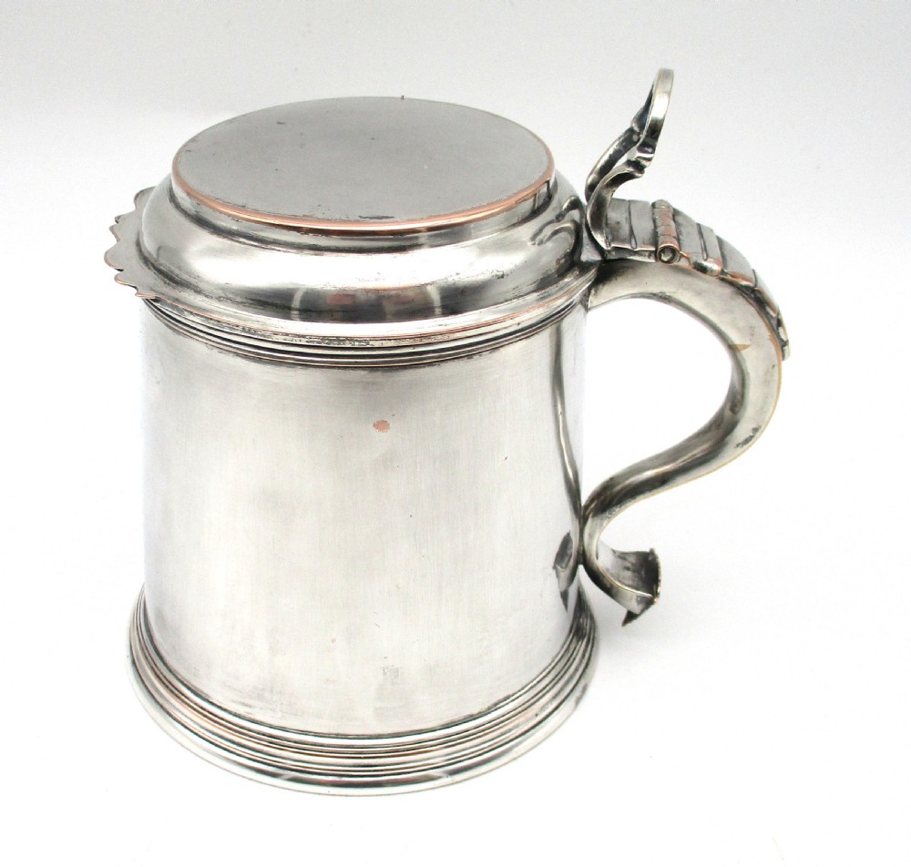 A late 18th-century silver-plated pint tankard featuring a hinged stepped lid, thumbpiece lever, curved scroll handle, and subtle copper exposure along worn rim edges.