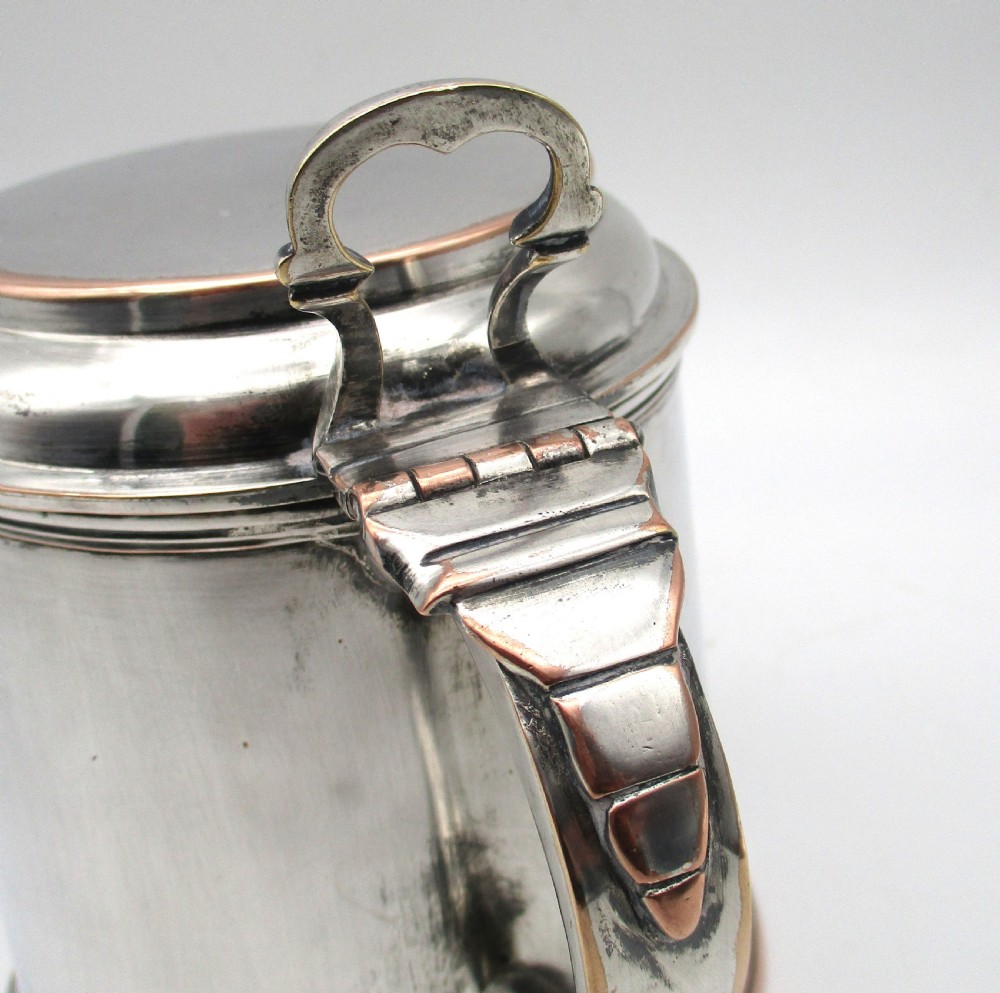 A late 18th-century silver-plated pint tankard featuring a hinged stepped lid, thumbpiece lever, curved scroll handle, and subtle copper exposure along worn rim edges. View IV