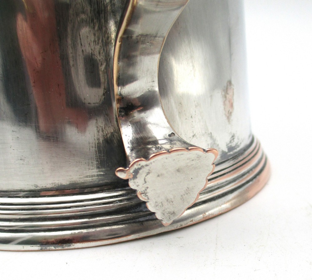 A late 18th-century silver-plated pint tankard featuring a hinged stepped lid, thumbpiece lever, curved scroll handle, and subtle copper exposure along worn rim edges. View V