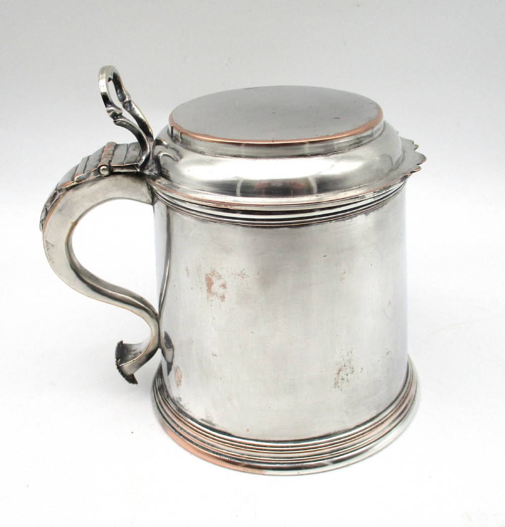 A late 18th-century silver-plated pint tankard featuring a hinged stepped lid, thumbpiece lever, curved scroll handle, and subtle copper exposure along worn rim edges. View VI