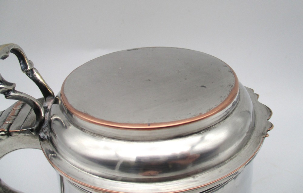 A late 18th-century silver-plated pint tankard featuring a hinged stepped lid, thumbpiece lever, curved scroll handle, and subtle copper exposure along worn rim edges. View VII