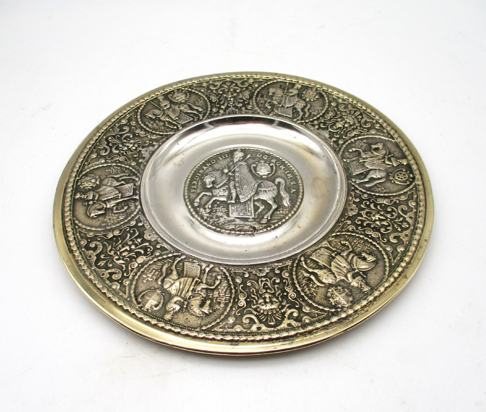 A circular 19th-century silver-plated bronze platter featuring a central relief profile of Emperor Ferdinand III on horseback surrounded by detailed equestrian vignettes and ornate scrolling foliage.