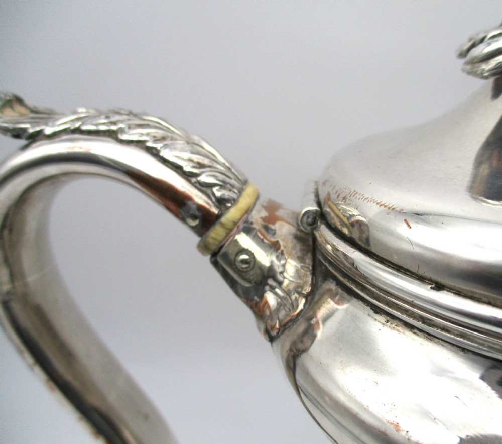 A Regency period Old Sheffield plated silver coffee pot featuring a baluster-shaped body, goose-neck spout, foliate finial, and scroll handle with heat insulators. View IV