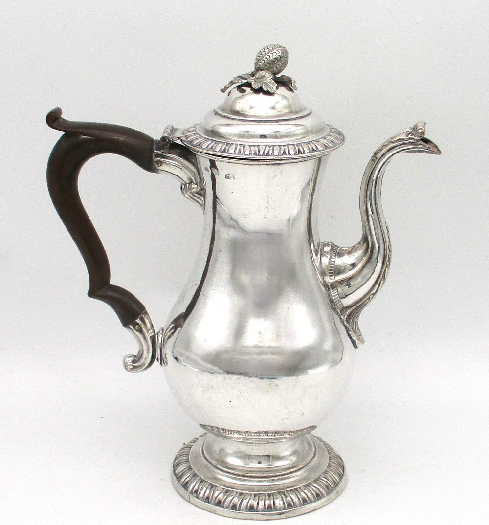 An eighteenth-century Sheffield silver-plated coffee pot featuring a baluster body, carved dark wood handle, fluted spout, and pineapple finial.