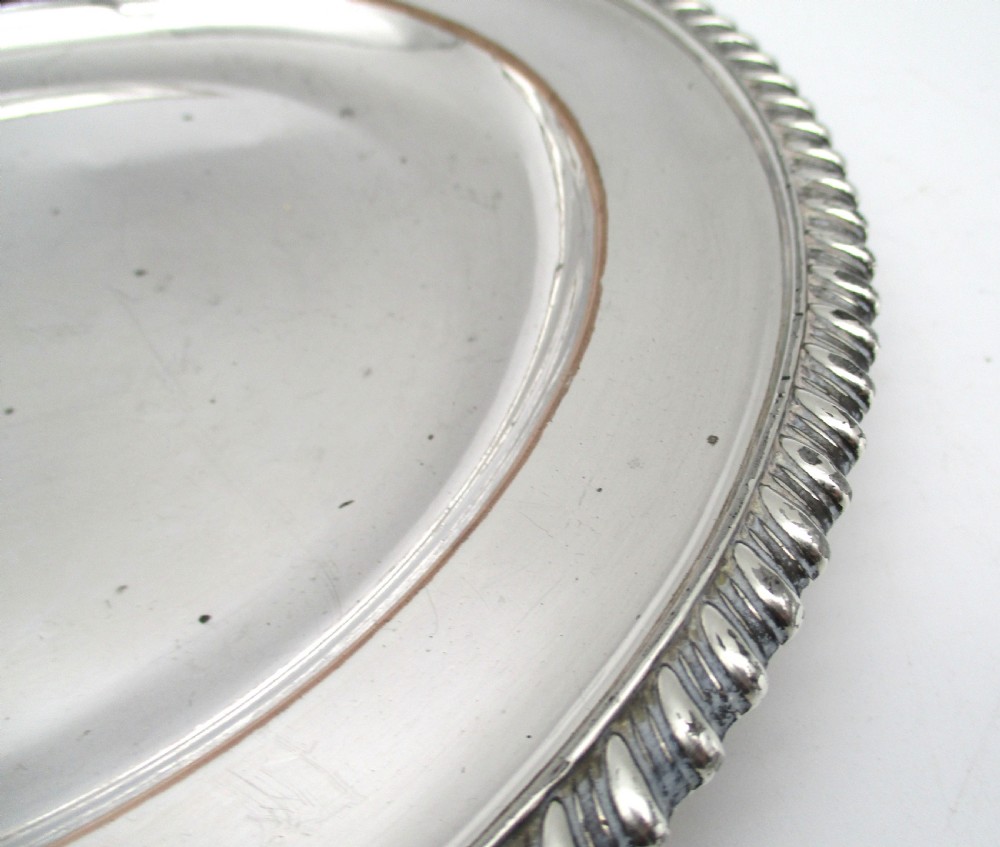 A circular Georgian Old Sheffield silver-plated dinner plate featuring a gadrooned rope-twist rim and an engraved armorial crest on the edge. View III