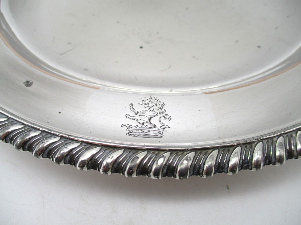 A circular Georgian Old Sheffield silver-plated dinner plate featuring a gadrooned rope-twist rim and an engraved armorial crest on the edge. View V