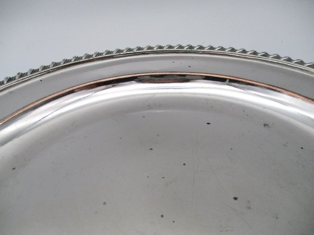 A circular Georgian Old Sheffield silver-plated dinner plate featuring a gadrooned rope-twist rim and an engraved armorial crest on the edge. View VI