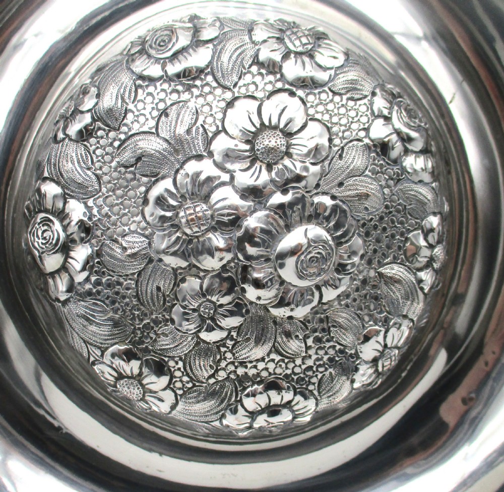 A circular silver-plated antique charger featuring an embossed floral rim and a raised central dome adorned with floral relief patterns. View III