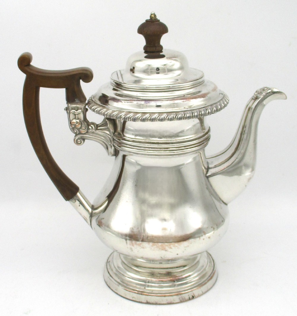 An antique Regency silver-plated coffee pot featuring a carved wooden handle, a gadrooned rim, and a stepped circular base.