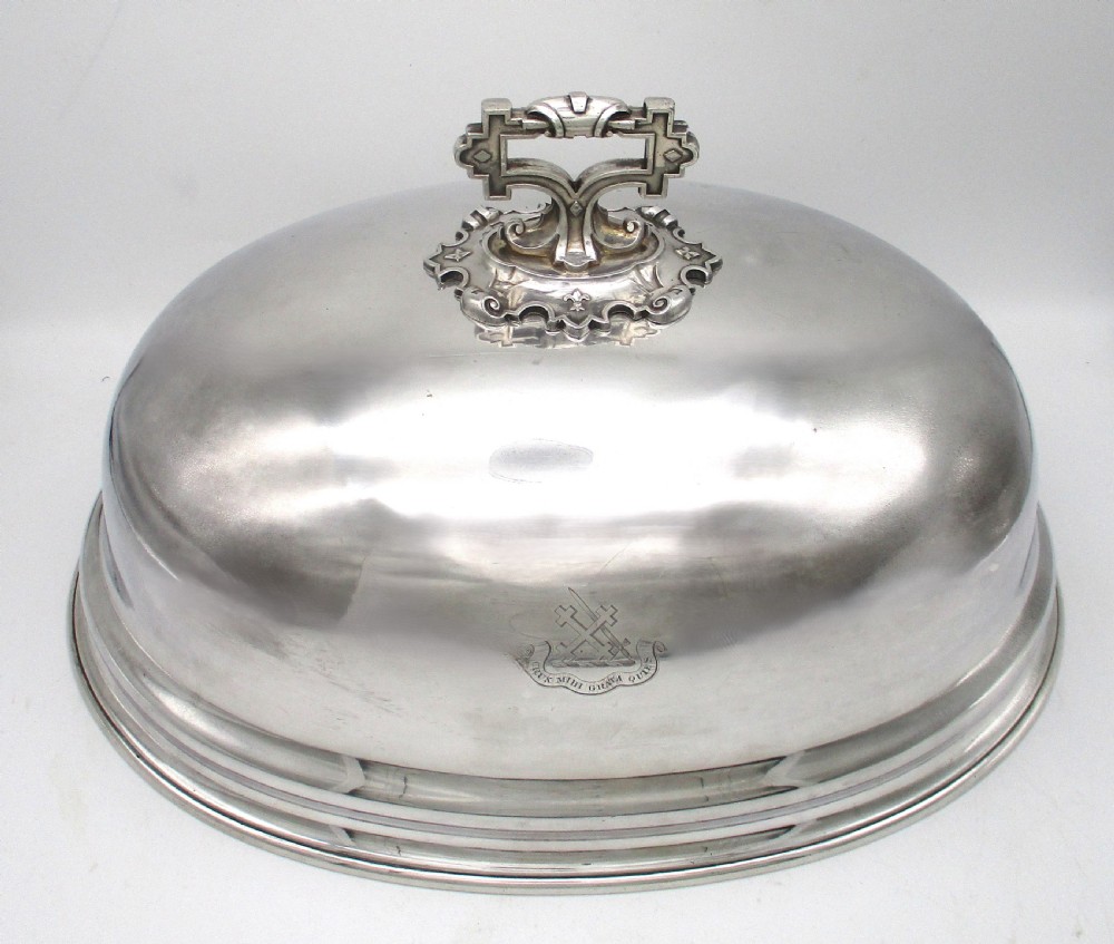 An oval Old Sheffield Plated meat dome featuring a moulded rim, an engraved crest, and a cast scrolling handle.
