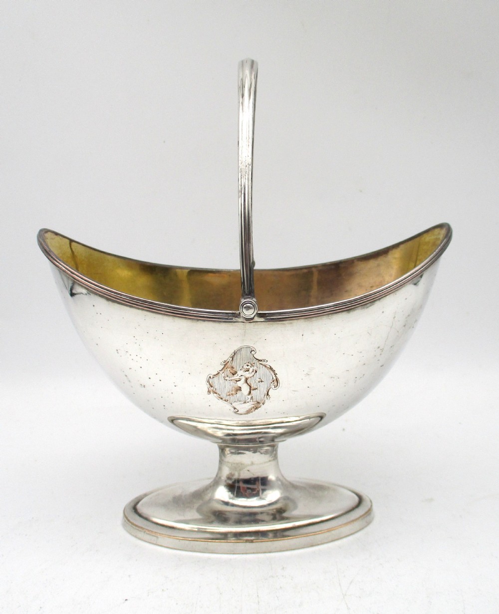 An eighteenth-century boat-shaped silver plated sweetmeat basket featuring a pedestal base, swing handle, heraldic crest engraving, and a gilded interior. View II