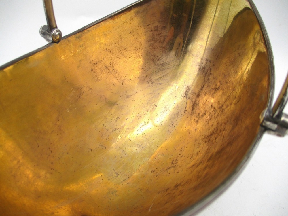 An eighteenth-century boat-shaped silver plated sweetmeat basket featuring a pedestal base, swing handle, heraldic crest engraving, and a gilded interior. View VII