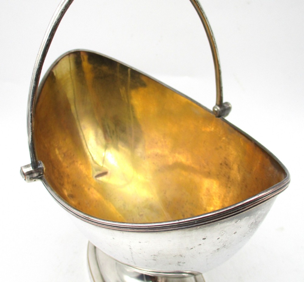 An eighteenth-century boat-shaped silver plated sweetmeat basket featuring a pedestal base, swing handle, heraldic crest engraving, and a gilded interior. View VIII