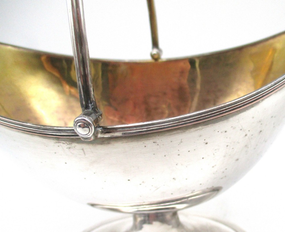 An eighteenth-century boat-shaped silver plated sweetmeat basket featuring a pedestal base, swing handle, heraldic crest engraving, and a gilded interior. View IX