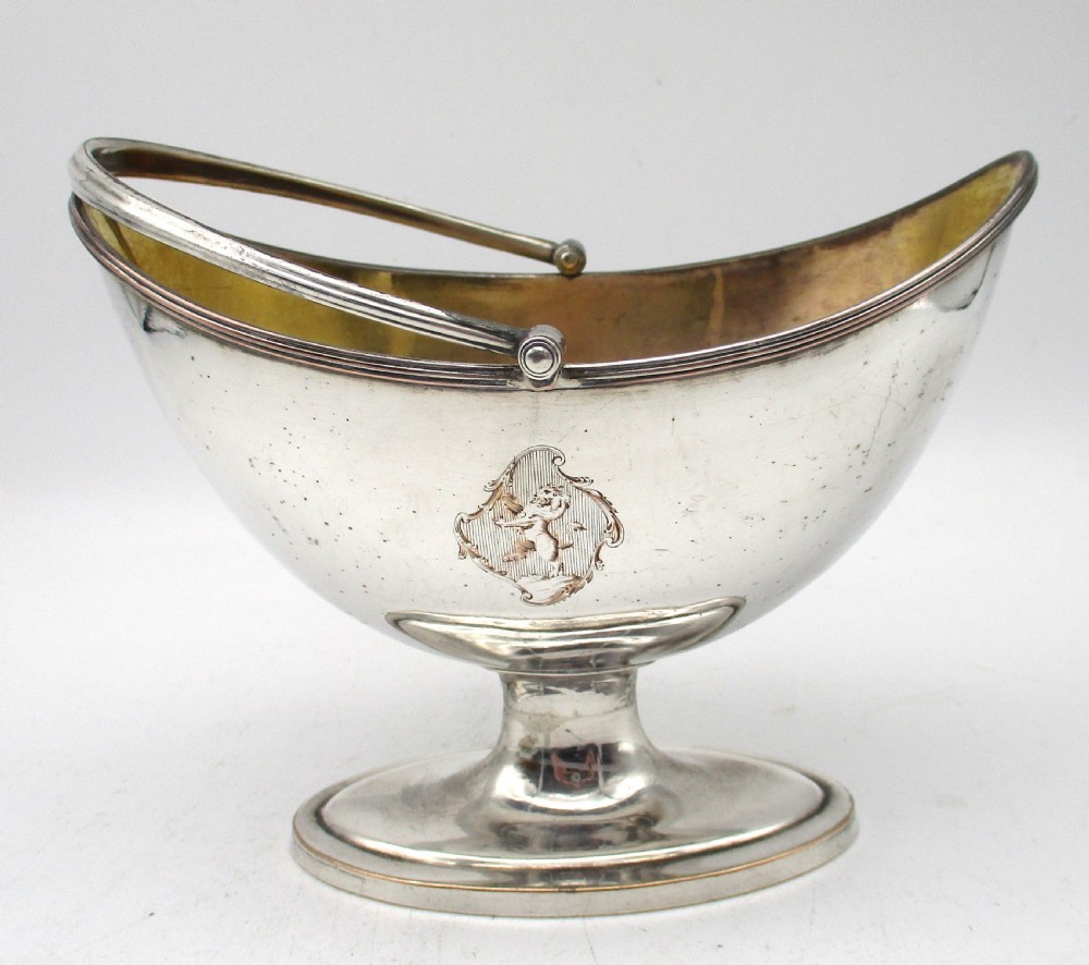 An eighteenth-century boat-shaped silver plated sweetmeat basket featuring a pedestal base, swing handle, heraldic crest engraving, and a gilded interior. View XI