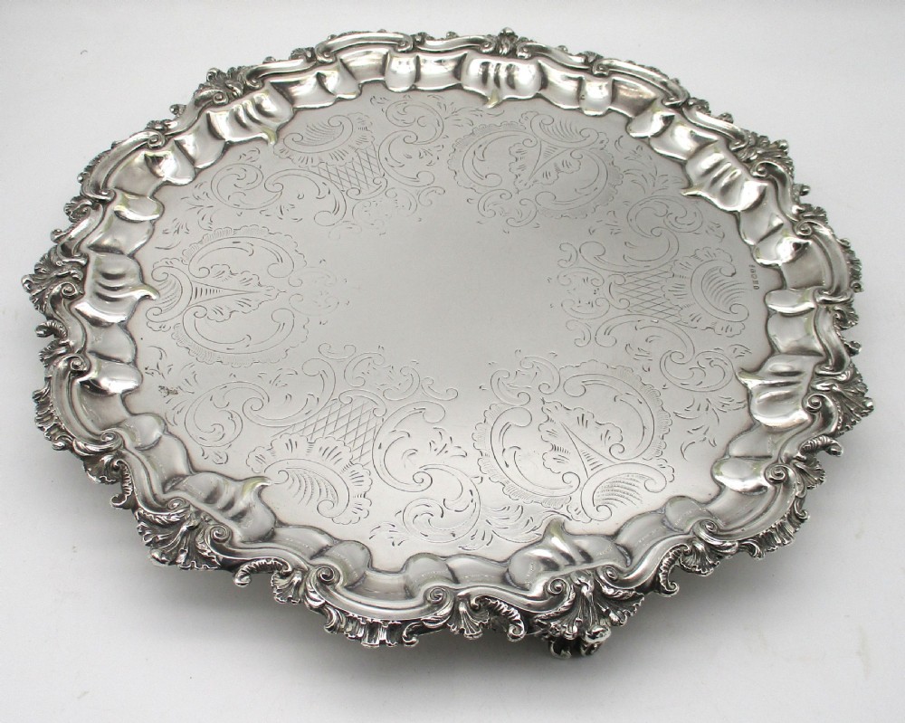 A circular Victorian silver-plated salver featuring an engraved floral scroll centre, shell-and-scroll moulded border, and short cast feet. View II