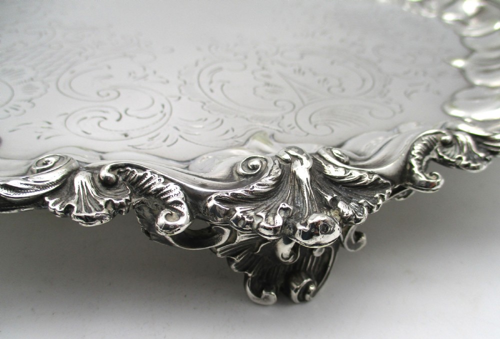 A circular Victorian silver-plated salver featuring an engraved floral scroll centre, shell-and-scroll moulded border, and short cast feet. View III