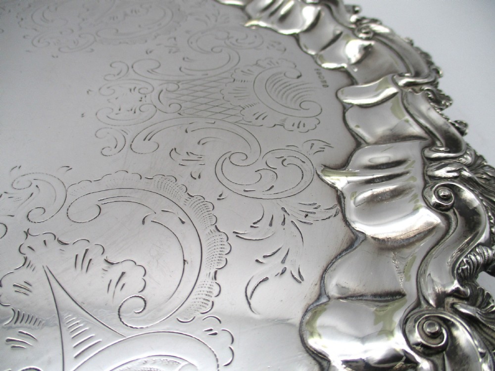 A circular Victorian silver-plated salver featuring an engraved floral scroll centre, shell-and-scroll moulded border, and short cast feet. View IV
