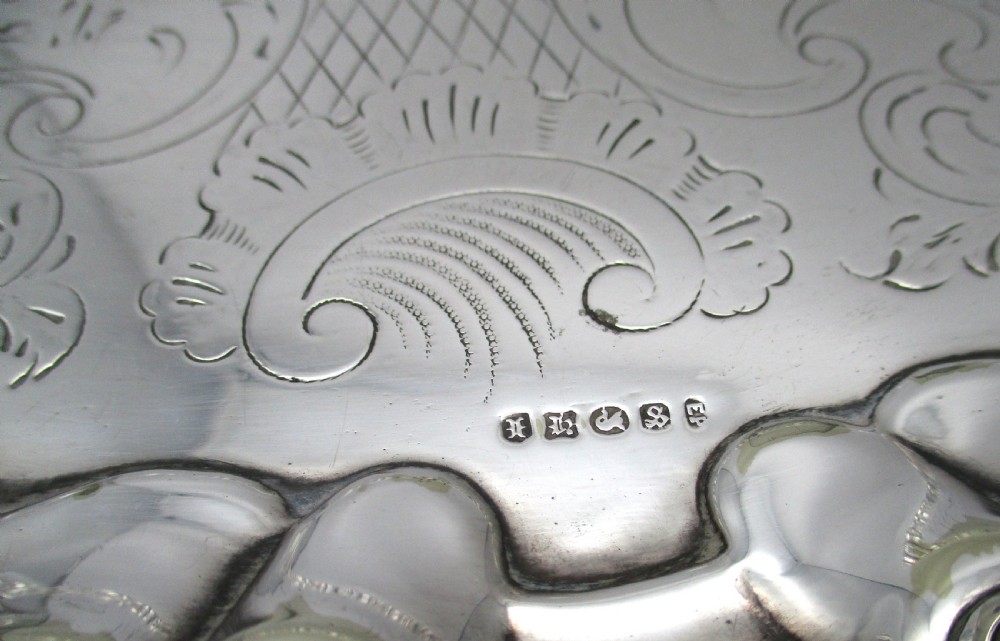 A circular Victorian silver-plated salver featuring an engraved floral scroll centre, shell-and-scroll moulded border, and short cast feet. View V