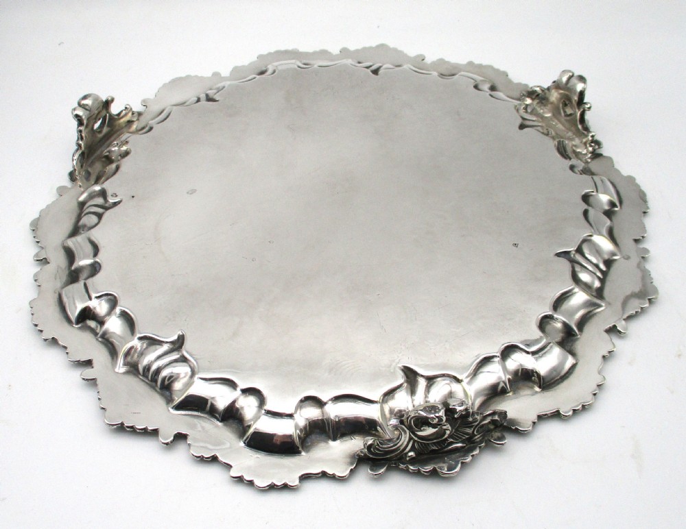 A circular Victorian silver-plated salver featuring an engraved floral scroll centre, shell-and-scroll moulded border, and short cast feet. View VII