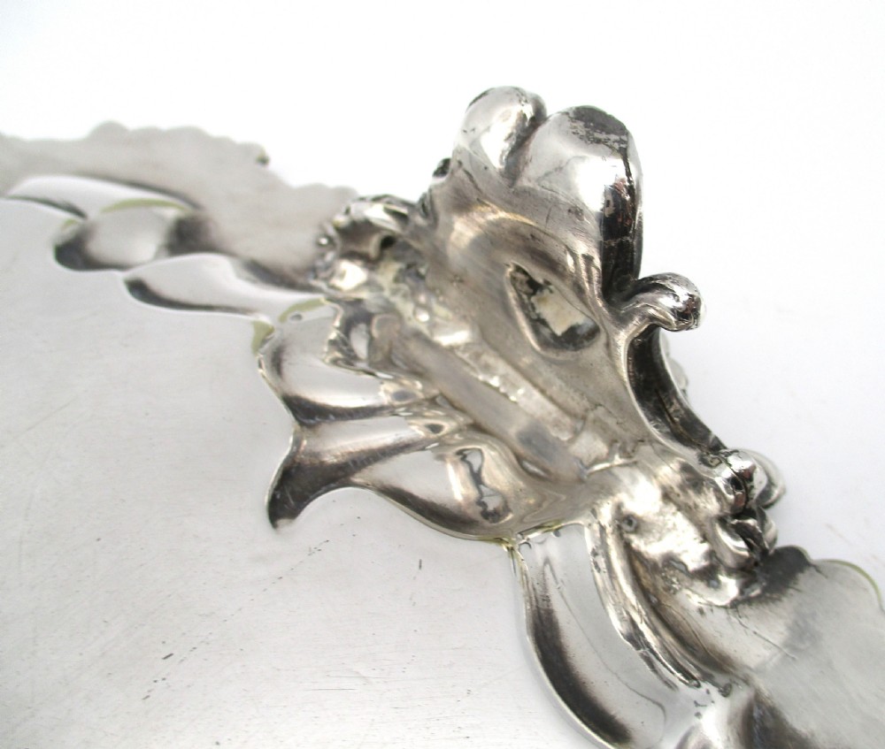 A circular Victorian silver-plated salver featuring an engraved floral scroll centre, shell-and-scroll moulded border, and short cast feet. View VIII