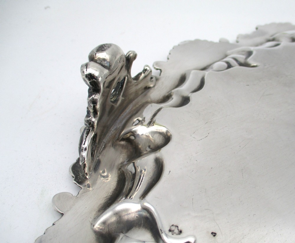 A circular Victorian silver-plated salver featuring an engraved floral scroll centre, shell-and-scroll moulded border, and short cast feet. View X
