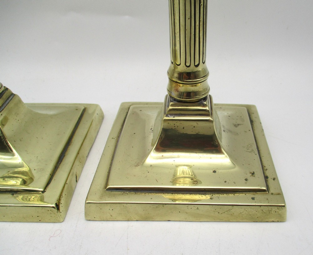 A pair of antique brass column candlesticks featuring fluted lower shafts and stepped square bases. View V