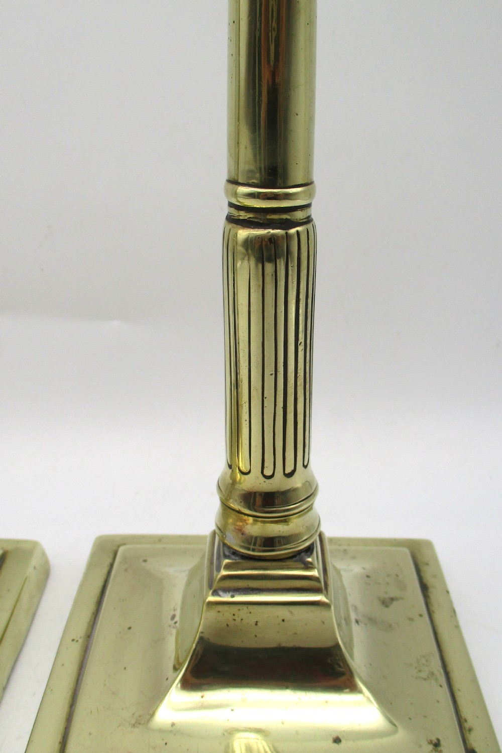 A pair of antique brass column candlesticks featuring fluted lower shafts and stepped square bases. View VI