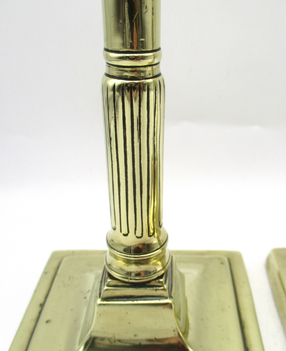 A pair of antique brass column candlesticks featuring fluted lower shafts and stepped square bases. View VII