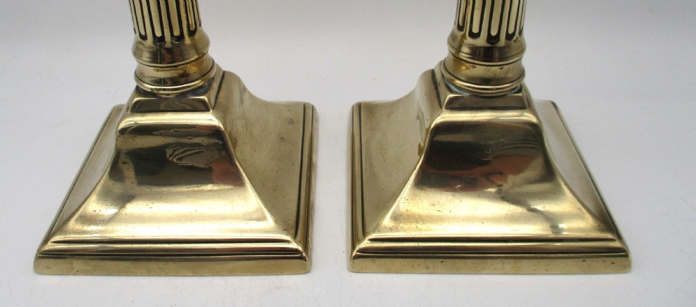 A pair of antique brass column candlesticks featuring fluted shafts and stepped square bases. View IV