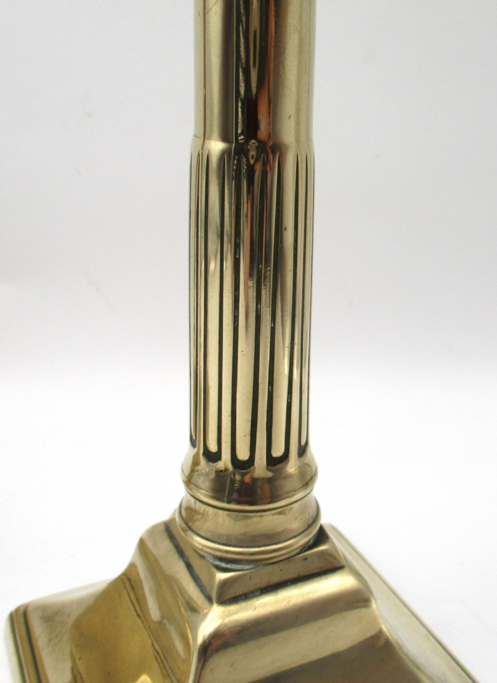 A pair of antique brass column candlesticks featuring fluted shafts and stepped square bases. View VII