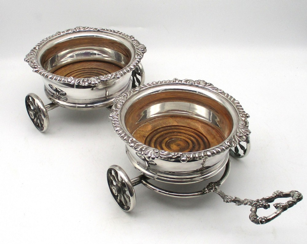 A pair of 19th-century silver-plated decanter coasters mounted on a wheeled carriage trolley with turned wooden bases and a decorative handle.