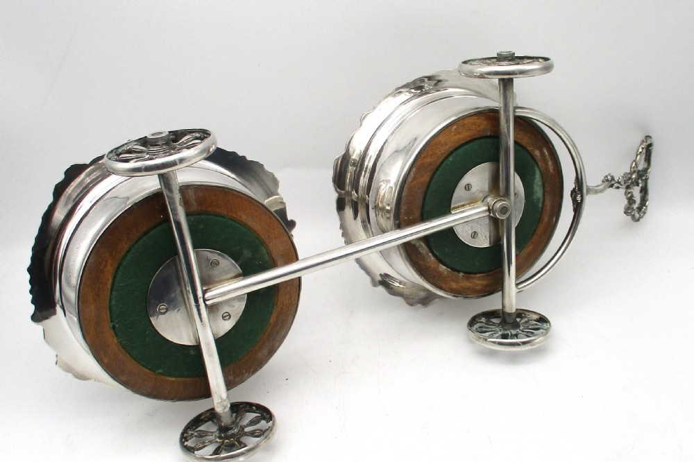 A pair of 19th-century silver-plated decanter coasters mounted on a wheeled carriage trolley with turned wooden bases and a decorative handle. View X